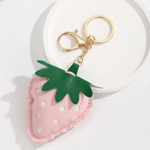 Pink PU leather strawberry keychain with gold clasp and green leaves on white plate