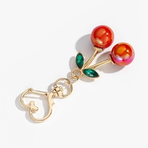 Macro detail of red pearlescent cherry keychain with green gems and gold heart clasp