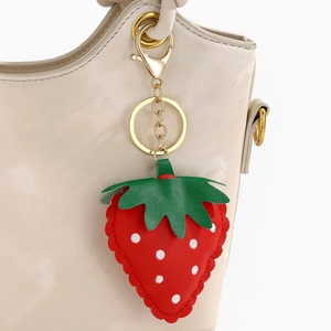 Detail view of a cute PU leather strawberry keychain with gold hardware on a beige bag