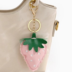 Close-up of pink leather strawberry keychain with gold hardware on a beige bag