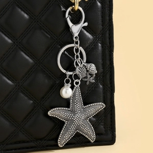 Detail of bohemian starfish and pearl keychain hanging on a black quilted leather bag