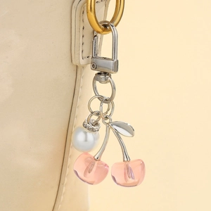 Detail of pink resin cherry keychain with pearl accent on a beige leather handbag