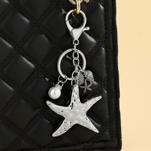 Detail of silver starfish keychain with faux pearl and shell charms on black leather bag