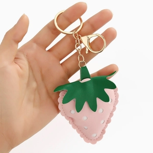 Detail of hand holding a cute strawberry leather keychain with golden hardware