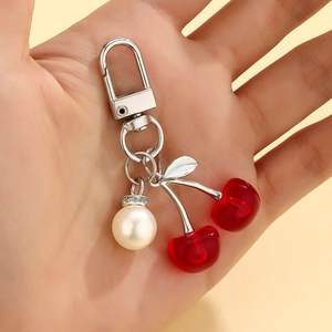 Detail of red cherry pendant keychain with pearl bead and metallic leaf on silver hook