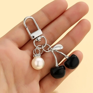Handheld view of black cherry keychain with white pearl accent and silver metal hook