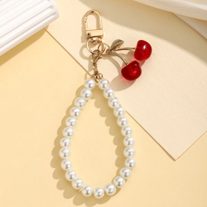 Close-up of pearl chain keychain with red cherry charm and golden metal leaf detail