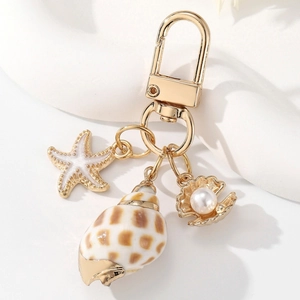 Detail of a gold starfish and seashell keychain with a pearl on a white wave stand
