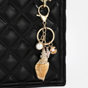 Detail of nautical keychain with natural spiral conch shell and white pearl on black leather