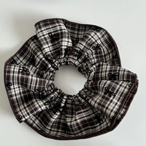 Brown and white plaid hair scrunchie with embroidered black bows on white background