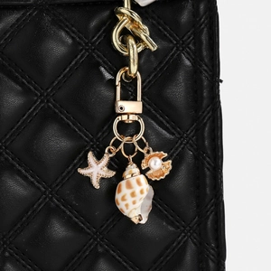 Detailed shot of ocean-themed gold keychain with starfish and shell on a black quilted bag