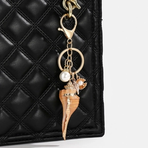 Detail of seashell keychain with pearls on a black quilted leather bag with gold clip