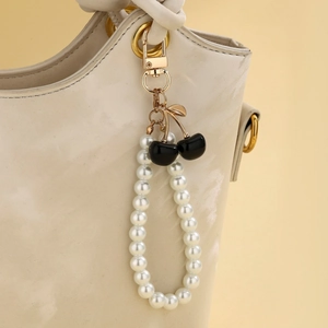 Detailed view of pearl cherry charm with gold clasp hanging on a beige bucket bag