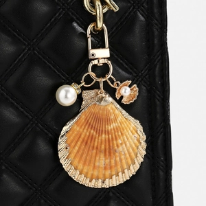 Detail of a natural shell keychain with gold edges and pearl on a black quilted bag