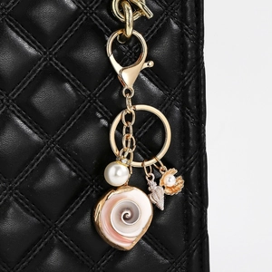 Detail of seashell and starfish keychain with large spiral conch on a black quilted bag