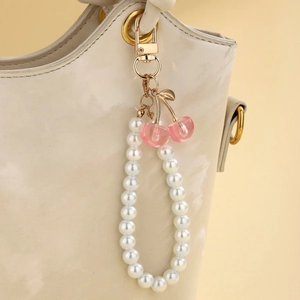 Close-up of pearl cherry keychain with pink resin drops and gold clasp on a handbag