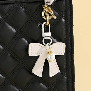 Detailed view of white leather bow charm with faux pearl on black quilted handbag