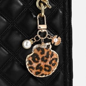 Macro shot of a leopard print shell pendant with large pearl on a black leather bag