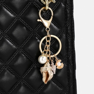 Detail view of a gold ocean keychain with shells and pearls on a black leather bag