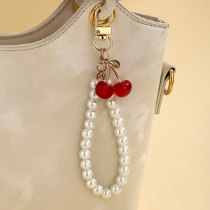 Detail of white pearl cherry charm pendant hanging on a cream leather handbag