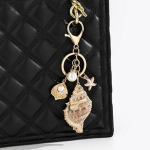 Detailed view of sea shell charm with gold trim and pearl on a black quilted bag