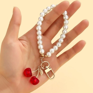 Close-up of pearl wrist strap with red cherry pendant and gold spring clasp detail
