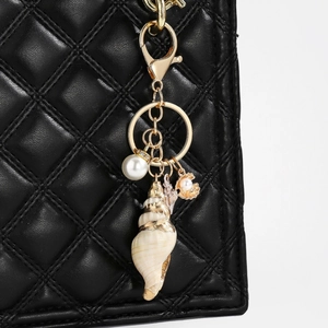 Detail of nautical keychain with natural spiral shell and pearl on black quilted bag