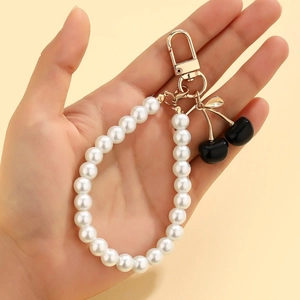 Detail view of pearl cherry keychain with black charms and gold D-clasp held in hand