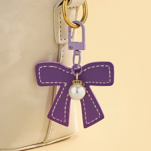 Detailed close-up of a purple leather bow keychain with pearl pendant and crystal accents