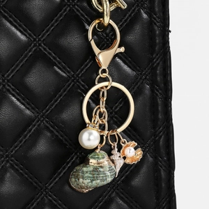 Detail of seashell keychain with pearl and starfish charms on a black quilted bag