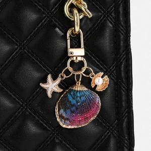 Detail of seashell keychain with starfish and pearl pendant on black quilted leather bag