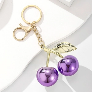 Exquisite purple cherry keychain with golden leaves and metallic mirror finish on white stand