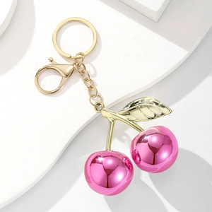 Polished magenta cherry keychain with golden leaves and lobster clasp on white background