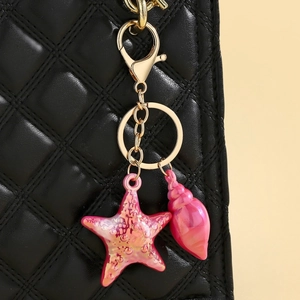 Nahaufnahme von rosa Seestern- und Muschelanhängern an einer schwarzen Stepptasche