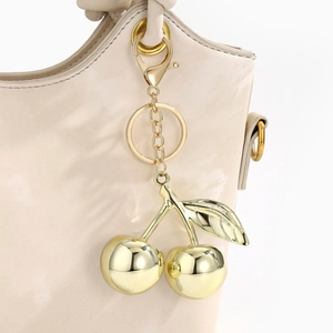 Close-up of golden cherry keychain accessory hanging on a beige leather handbag