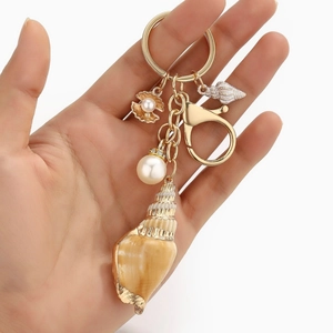 Detailed close-up of shell keychain with natural conch, pearl, and gold metal accents