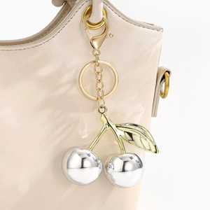 Detail of silver resin cherry keychain with gold leaves on a luxury apricot handbag