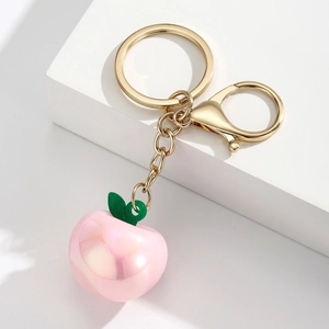 Close-up of pink peach keychain with green leaves and gold hardware on white pedestal