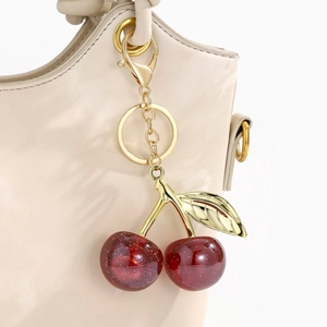 Detailed close-up of glittering cherry bag charm with golden leaves on leather bag