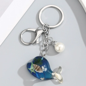 Détail d'un porte-clés baleine en résine bleue avec coquillages, perle et étoile de mer