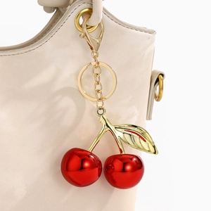 Close-up of vibrant red resin cherries keychain with gold leaf on a white leather bag