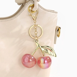 Close-up of a pink iridescent cherry keychain with golden leaves on a white leather bag