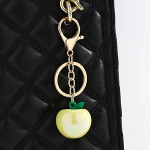 Detail of yellow apple charm with green leaf on black quilted bag with gold hardware