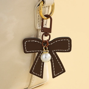 Detail view of brown leather bow charm with white stitching and pearl pendant