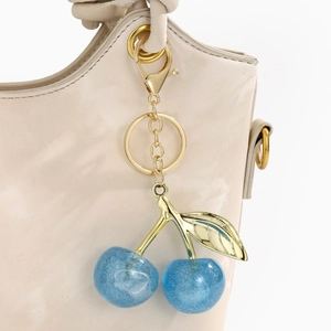 Detail of glittery dark blue cherry pendant hanging on a beige leather handbag