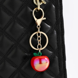 Close-up of a red apple keychain with gold metal clasp on a black quilted leather bag