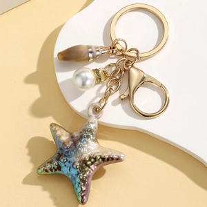 Detailed macro of a seashell and starfish charm keychain with a pearl accent and gold lobster clasp