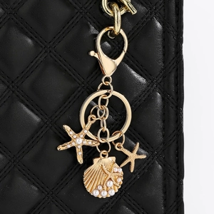 Detail of golden starfish and pearl shell keychain pendant on black quilted leather bag