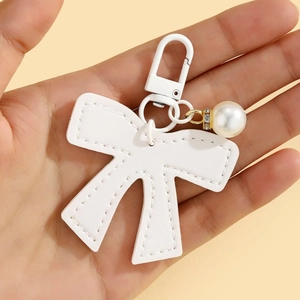 Detail of white leather bow keychain with pearl charm and metal clip held by hand