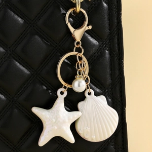 Detail of starfish and shell charms with pearls hanging on a black quilted leather bag